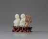 A pale jade carving of two boys with a wooden stand