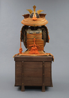 A large gilded Japanese ōyoroi with orange cords (hi’ito odoshi yoroi). A large hoshikabuto-helmet with gilded parts, large fukikaeshi