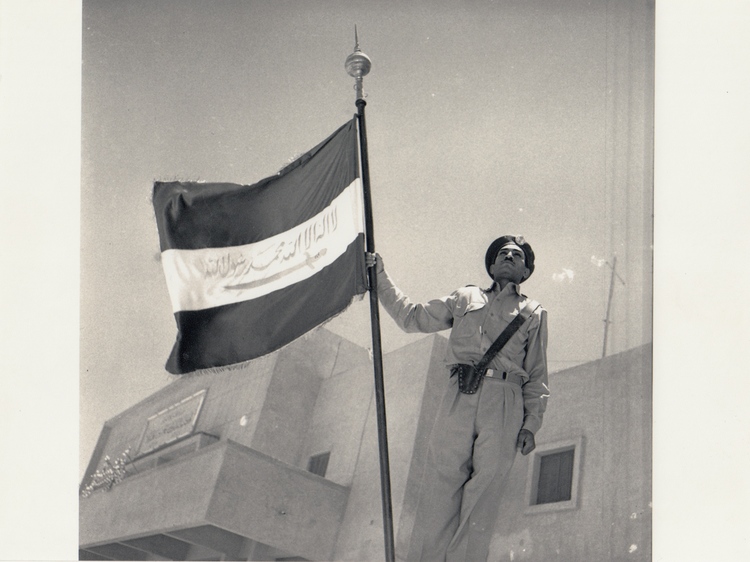 A RARE PHOTOGRAPH OF A PROUD STANDING SAUDI SOLDIER HOLDING AN UNIQUE SAUDI ARABIA FLAG, PROBABLY 1950