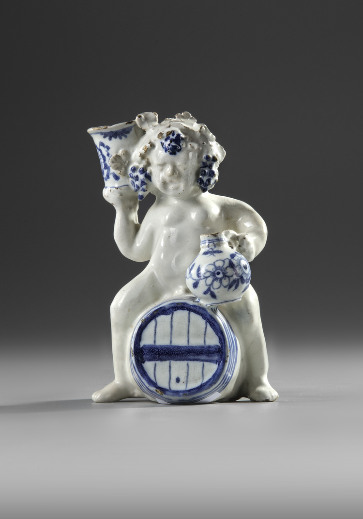 A BLUE AND WHITE BACCHUS ON A WINE BARREL, PROBABLY BRUSSELS 18TH CENTURY